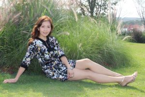 美丽的姐姐坐在湖边的草坪上展示她完美无瑕的长腿和美足